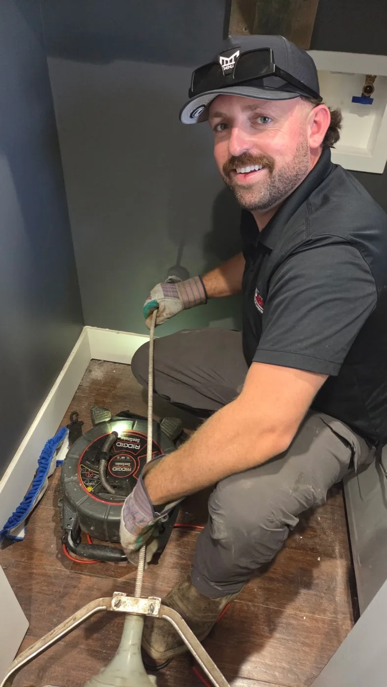 Floworx plumber working beside a drain-cleaning machine in a laundry room